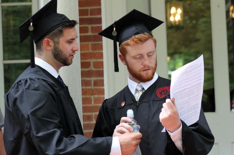 a group of men in graduation gowns and cap looking at paper