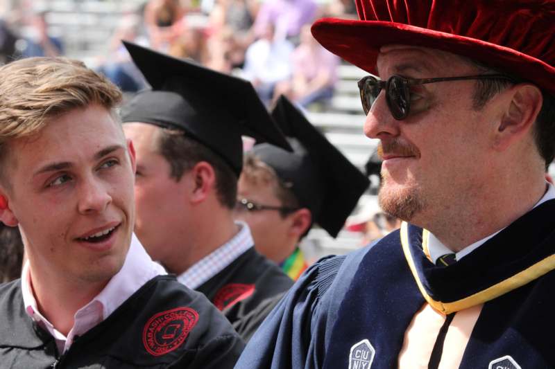 a man in a graduation gown and cap talking to another man