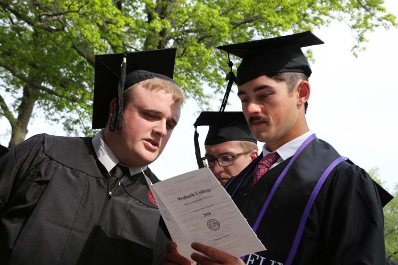 a group of men in graduation gowns and caps looking at a certificate