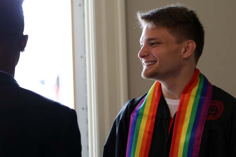 a man smiling with a rainbow scarf around his neck