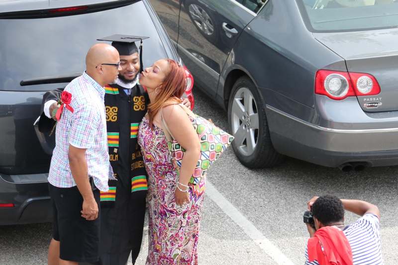 a man and woman in graduation gowns and cap kissing a woman