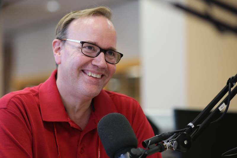 a man in a red shirt smiling at a microphone