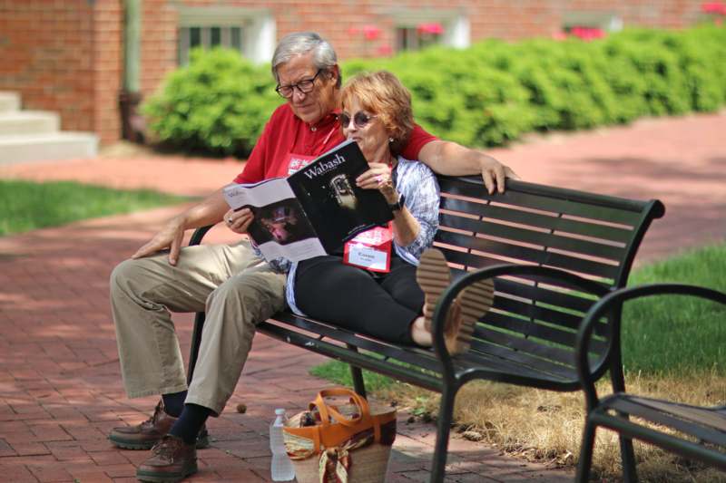 a man and woman sitting on a bench reading a book