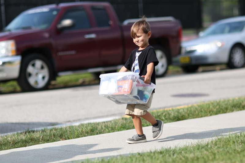 a boy walking on the sidewalk carrying a plastic container