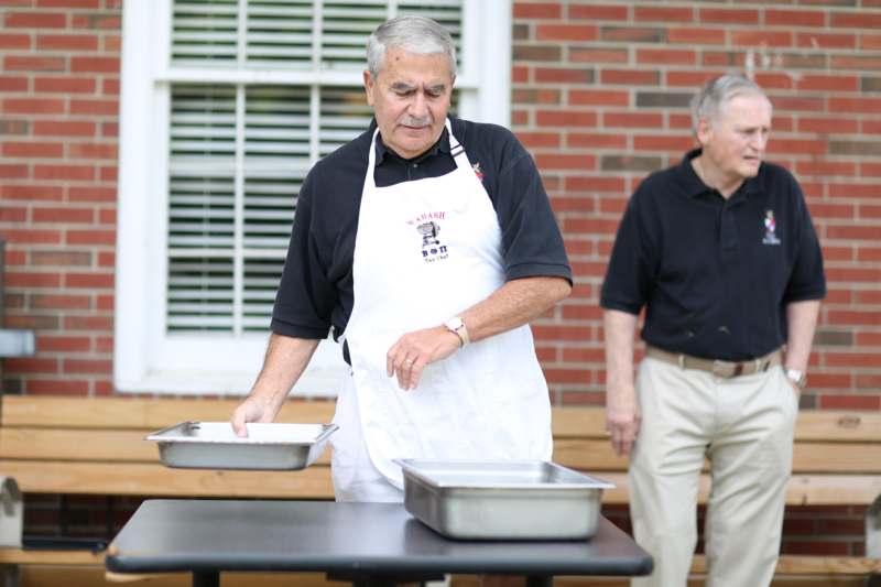 a man wearing an apron standing next to a table with two pans