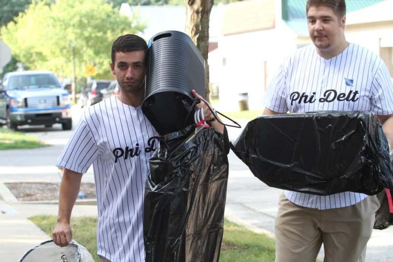 two men wearing baseball uniforms holding trash bags