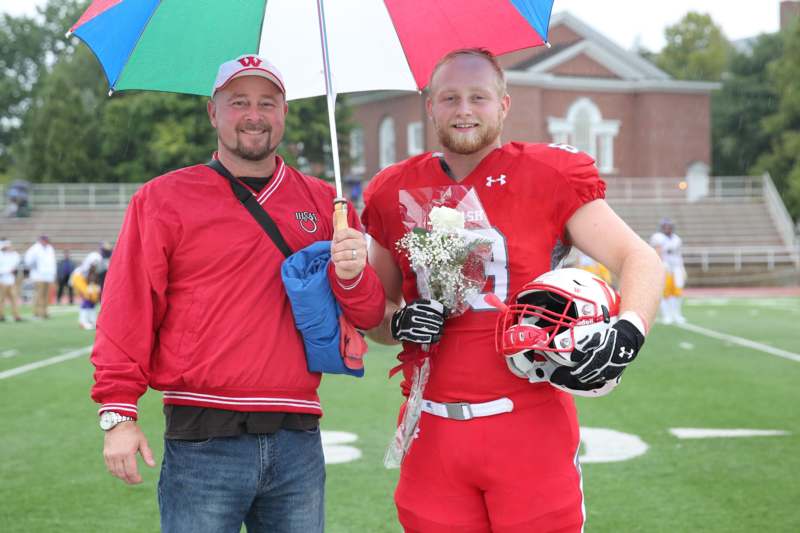 two men standing on a football field holding flowers and umbrella
