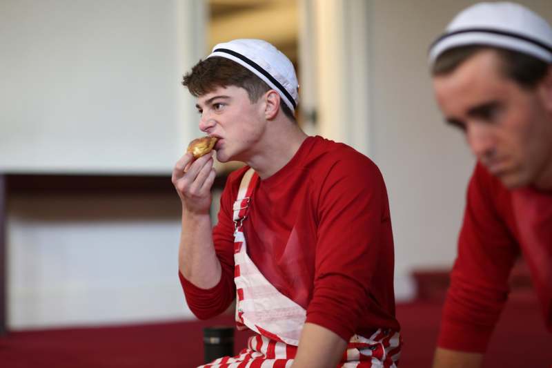 a man in red and white striped overalls eating a donut