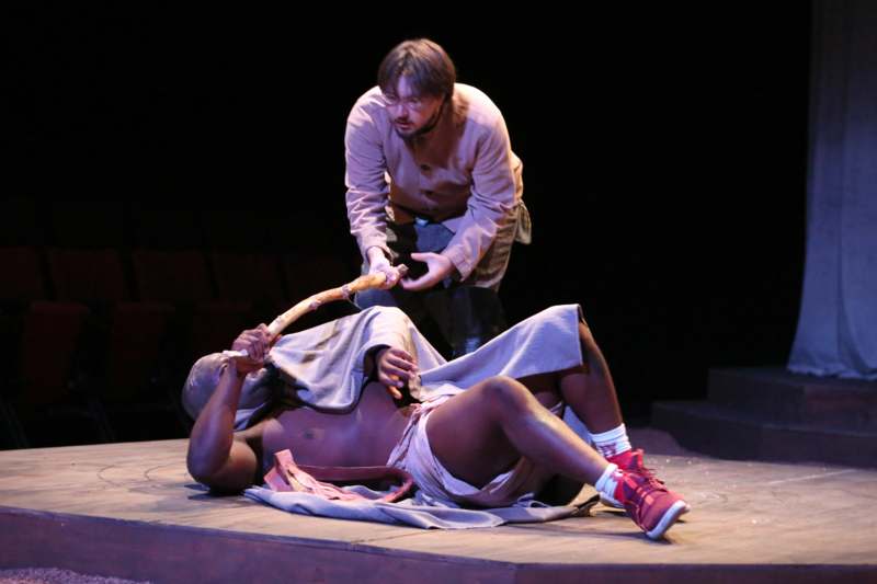 a man holding a stick to a man lying on a stage