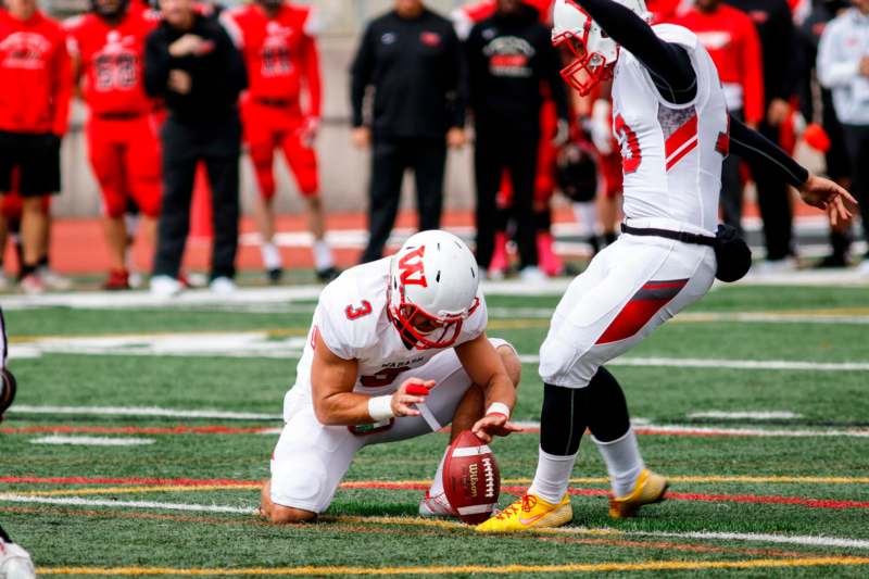 a football player kneeling on the ground with another football player in the background