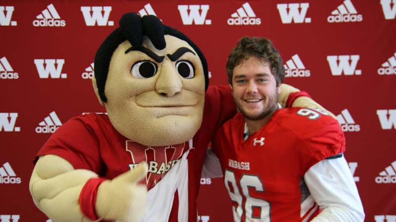 a man with a mascot posing with his arm around another man