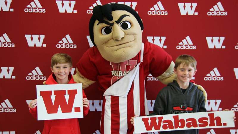 a two boys posing with a mascot