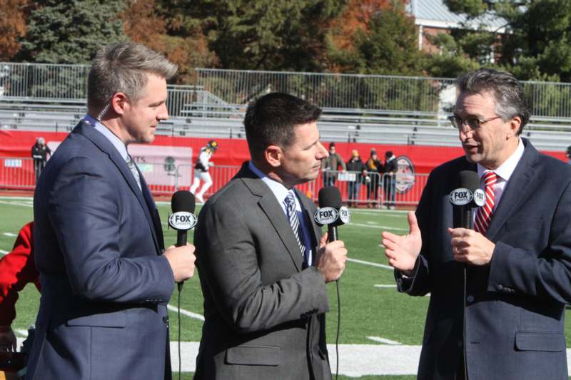 a group of men in suits talking into microphones on a football field
