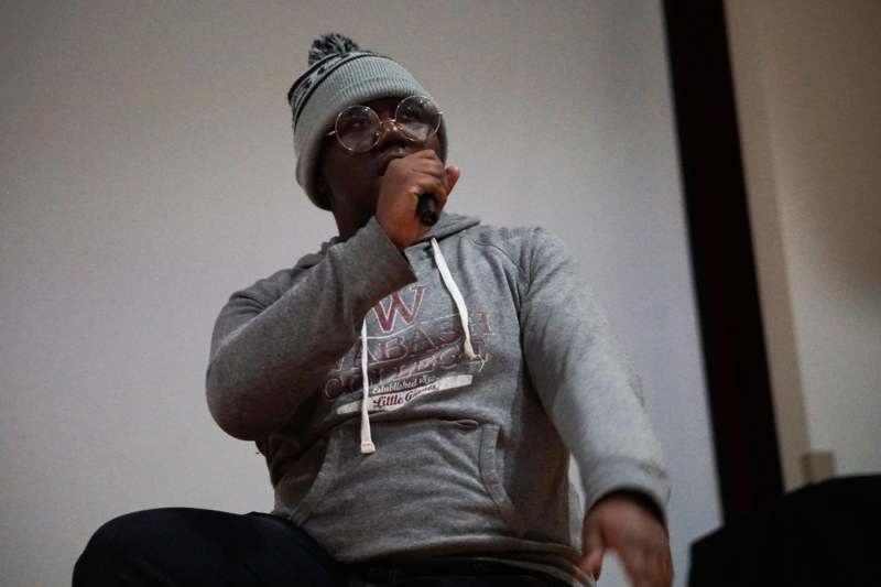 a man wearing glasses and a grey sweatshirt holding a microphone