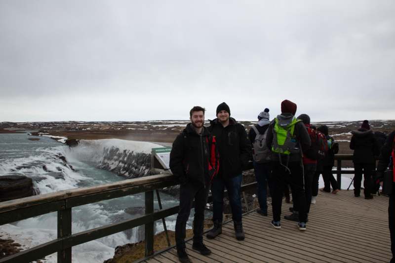a group of people standing on a bridge with a waterfall in the background