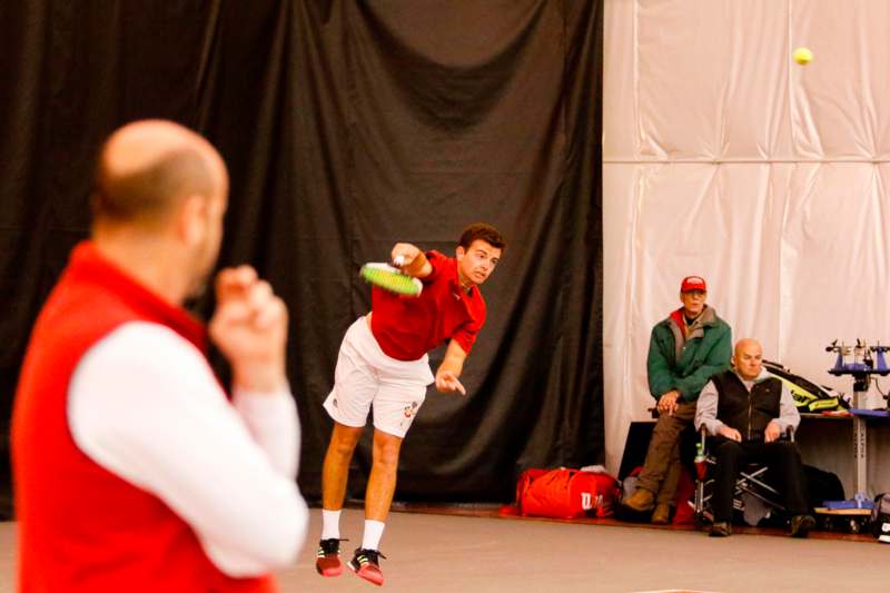 a man in red shirt and white shorts hitting a tennis ball with a racket