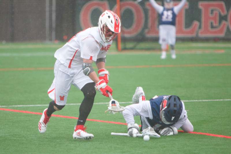 a man in a helmet holding a lacrosse stick while another man is lying on the ground
