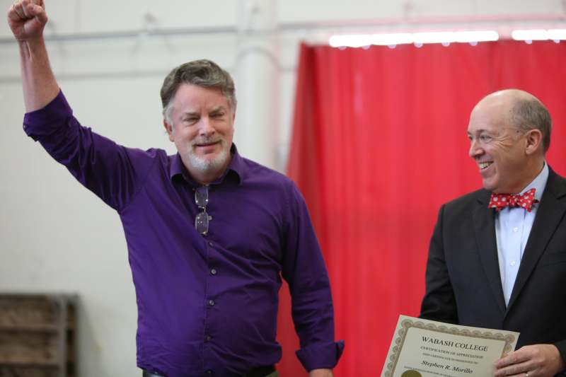 a man holding a certificate and pointing at another man