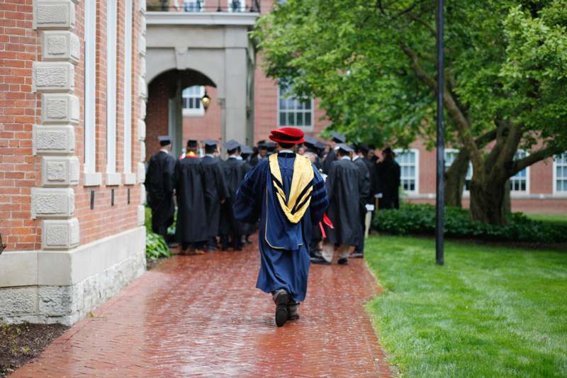 a man in a blue gown and hat walking down a brick path