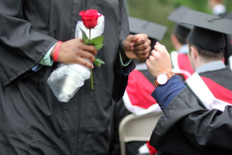 a person in a graduation gown holding a rose