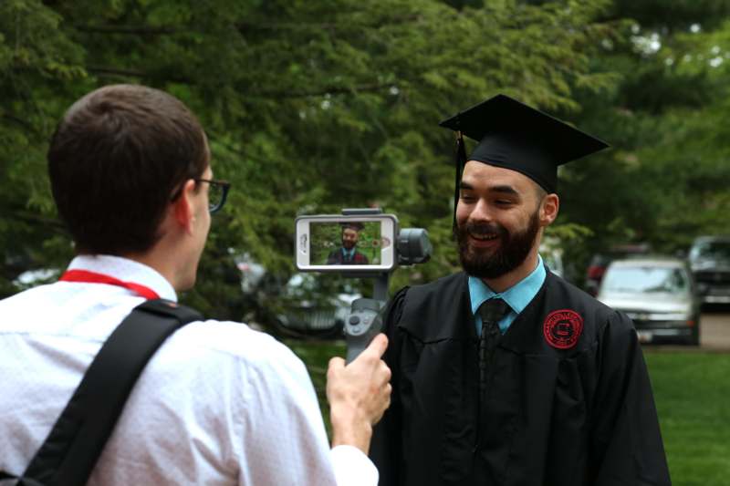 a man in a graduation gown taking a picture of a man
