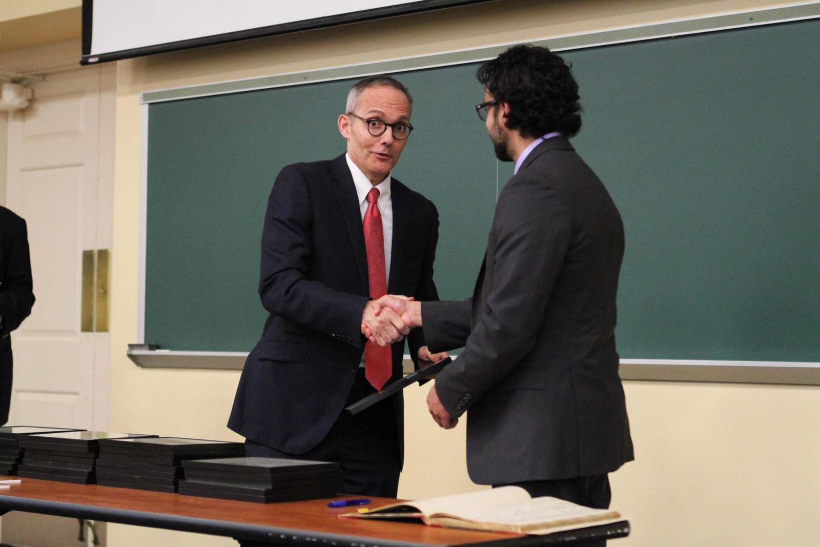 a man shaking hands with another man in front of a chalkboard