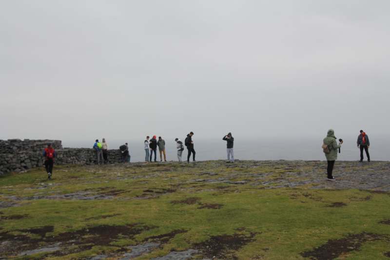 a group of people standing on a stone wall overlooking the ocean