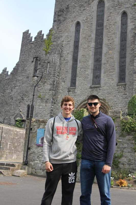 two men standing in front of a stone building