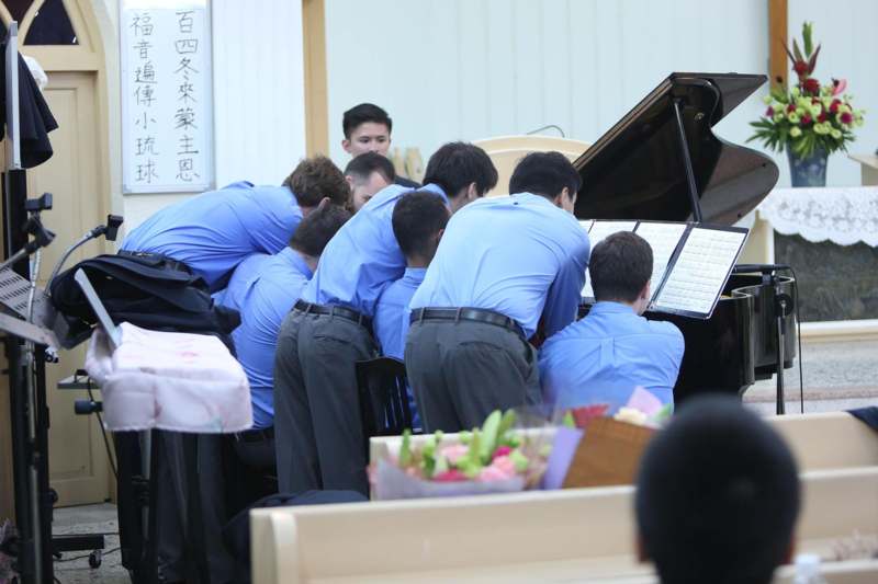 a group of people in a row playing a piano