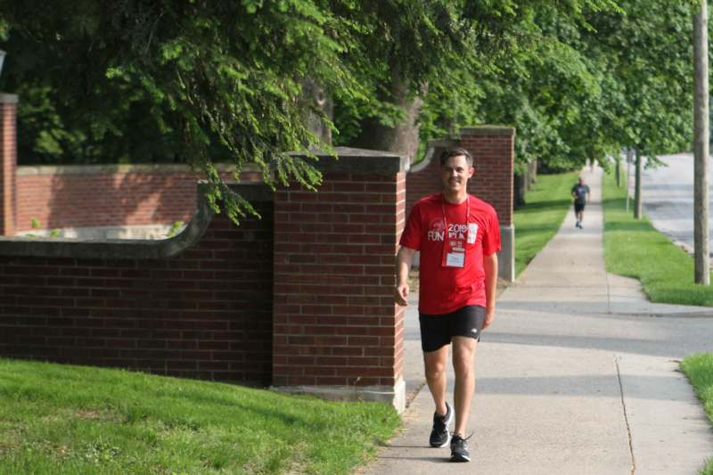 a man wearing a red shirt and shorts walking on a sidewalk