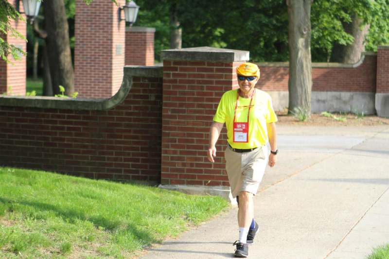 a man wearing a yellow shirt and sunglasses walking on a sidewalk