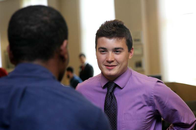 a man in a purple shirt and tie talking to another man