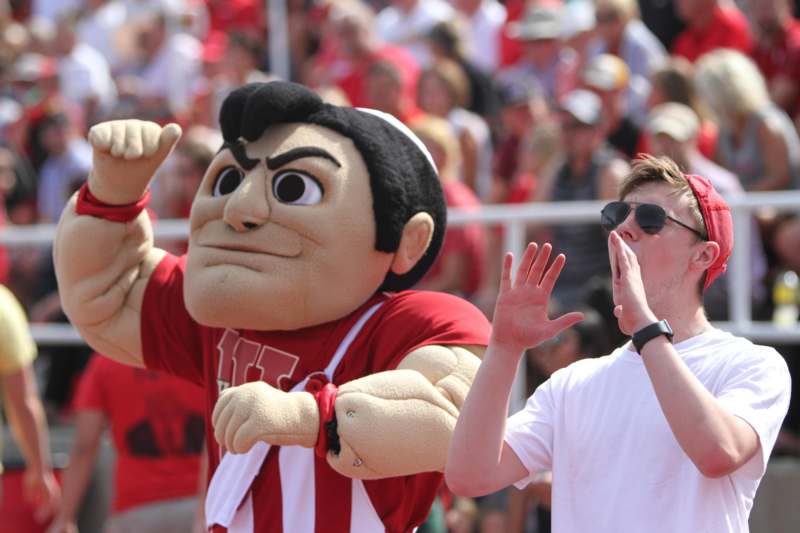a man in a white shirt and a large mascot in front of a crowd