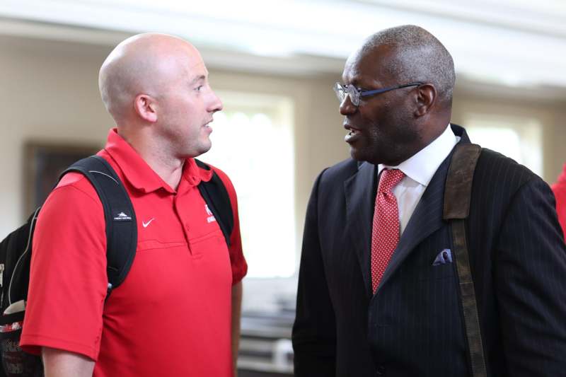 a man in a red shirt and black suit talking to another man
