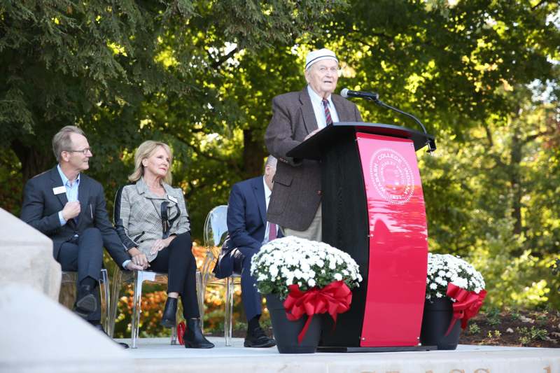 a man standing at a podium with a microphone and people sitting in chairs