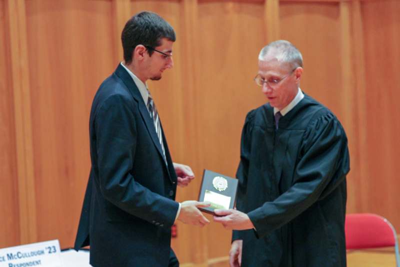 a man in a black robe handing a man a award to another man
