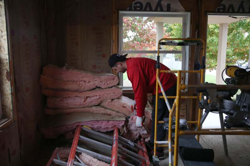 a man in a red shirt and black cap working on a stack of insulation