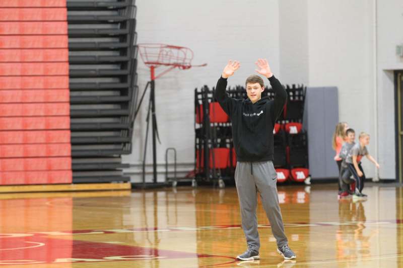 a man in a black hoodie holding his hands up in a gym