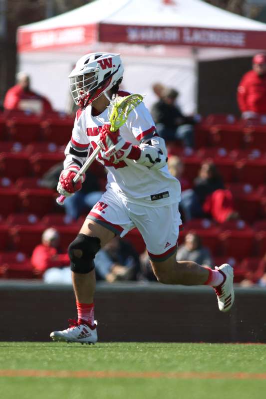 a man wearing a white and red uniform running with a lacrosse stick