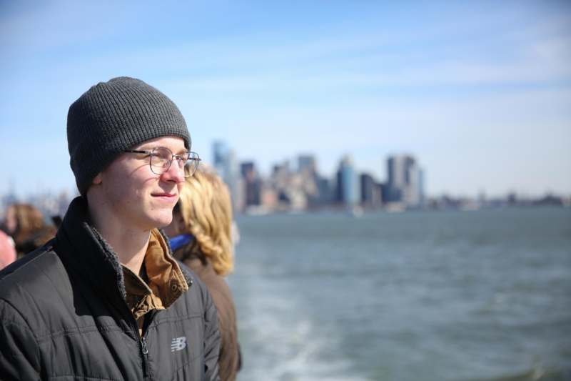 a man in a hat and glasses standing on a boat in front of water