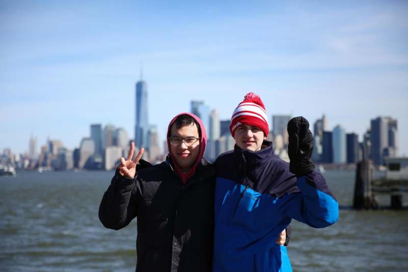 two men posing for a picture in front of water and city in the background