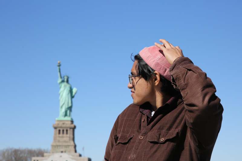 a man in a pink hat and glasses with a statue in the background
