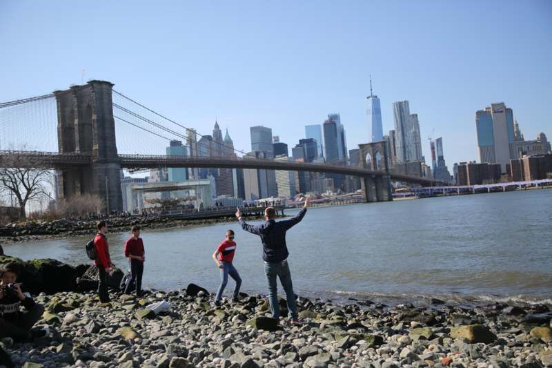 a group of people standing on a rocky beach with a bridge in the background