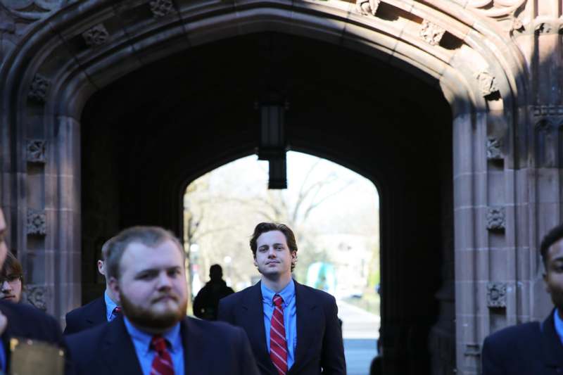 a group of men in suits walking under a stone archway