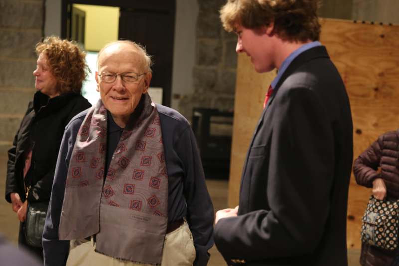 a man in glasses and a scarf talking to a man