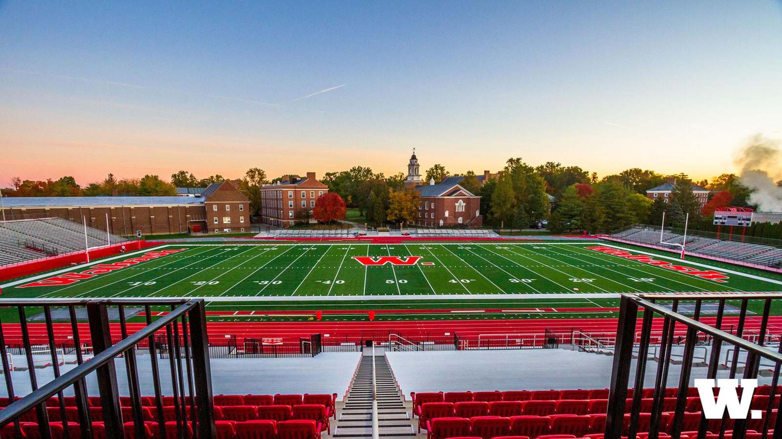 a football field with red seats and a building in the background