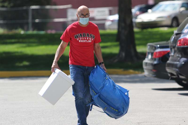 a man wearing a face mask carrying a bag and a plastic container