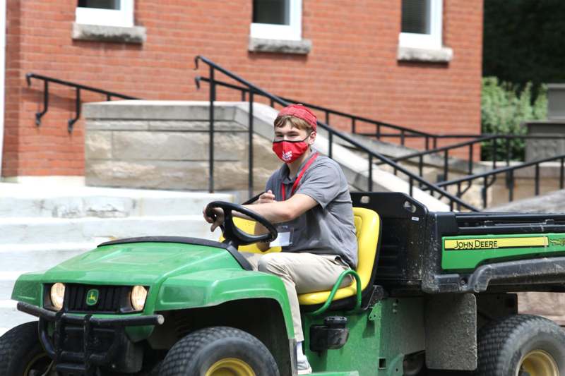 a boy wearing a face mask driving a tractor