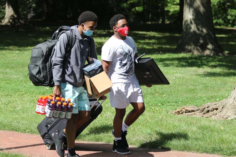 a couple of men wearing face masks walking with luggage