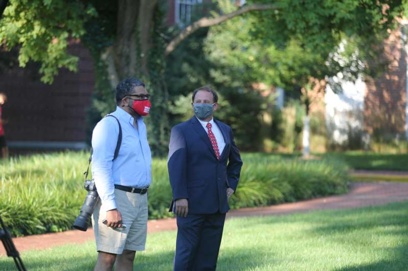 a man in a suit and a mask standing next to another man in a suit and a camera